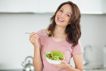 Portrait of smiling woman with a bowl of salad in kitchen