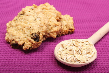 Oatmeal cookies and flakes on wooden spoon. Purple background