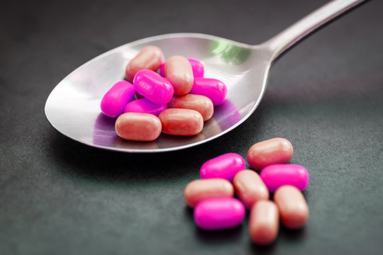 Pills or candy in spoon on dark background.