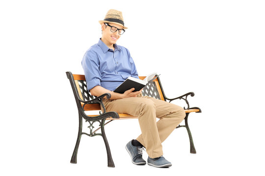 Young man with glasses reading a book on wooden bench