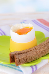 Boiled egg in egg cup on table on light background