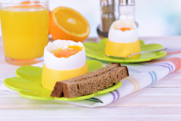 Boiled eggs in egg cups on table on light background