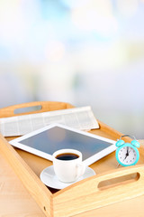 Tablet, newspaper, cup of coffee and alarm clock on wooden tray