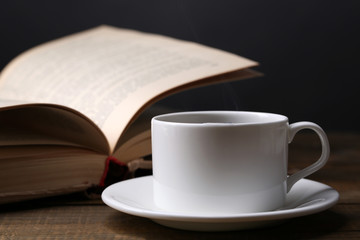 Cup of hot coffee with book on table on dark background