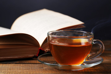 Cup of hot tea with book on table on dark background