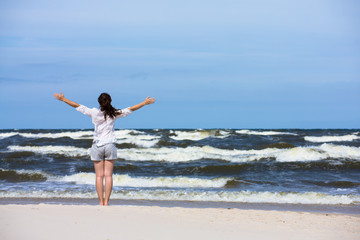 Fototapeta na wymiar Teenage girl standing on beach, arms up