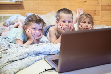 Pretty children looking at computer monitor while laying in bed