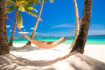 Straw hammock in the shadow of palm on tropical beach by sea