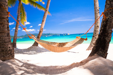 Straw hammock in the shadow of palm on tropical beach by sea