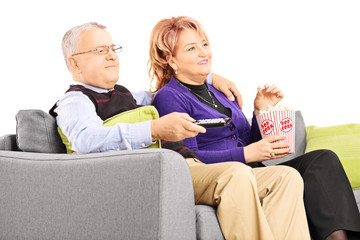 Mature couple watching TV and eating popcorn seated on a sofa