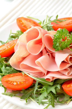 Sliced ham with arugula leaves and tomatoes