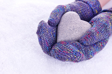 Female hands in mittens with heart on snow background