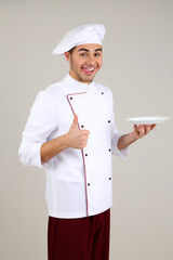 Professional chef in white uniform and hat, on gray background