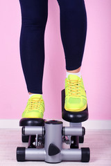 Woman doing exercise on stepper. Close-up on legs.