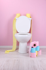 White toilet bowl and colorful rolls of toilet paper, in