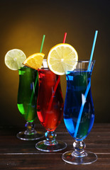 Glasses of cocktails on table on dark yellow background