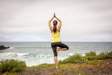 Fototapeta na wymiar Young woman practicing tree yoga pose near the ocean