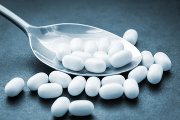 Pills in spoon on dark background. Color toned image.