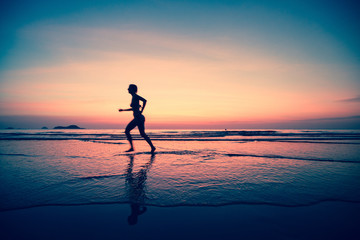 Silhouette of a woman jogger on the beach at sunset