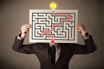 Businessman holding a paper with a labyrinth on it in front of h