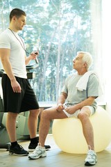 Personal trainer explains to a senior man how to do exercise 