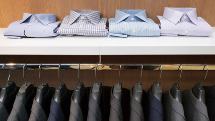 Row of men suit jackets on hangers and shelf with shirt in cloth