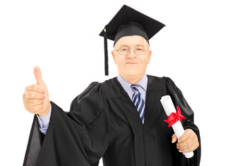 Mature man in graduation gown holding a diploma, giving thumb up