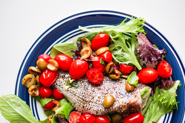 Baked seabass with tomatoes and basil on white background
