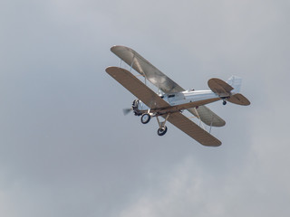 Obraz premium A Silver Biplane in Flight in a Blue Sky and Some Fluffy Clouds