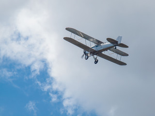 A Silver Biplane in Flight in a Blue Sky and Some Fluffy Clouds