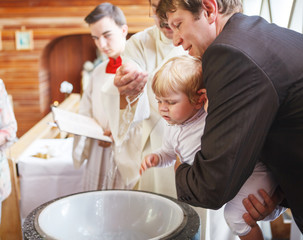 Little baby boy being baptized in catholic church holding by fat