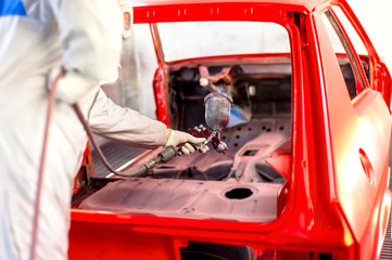 worker painting a red car in a special garage