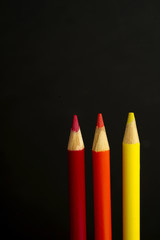 red, orange and yellow coloured pencil crayons on a black backgr