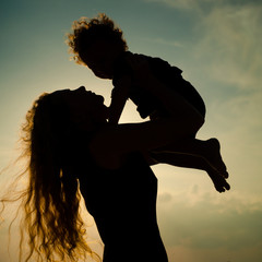 Mother and little son silhouettes on beach at sunset - obrazy, fototapety, plakaty