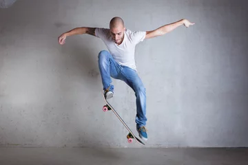 Abwaschbare Fototapete Skateboarder doing a skateboard trick - ollie - against concrete © PriceM