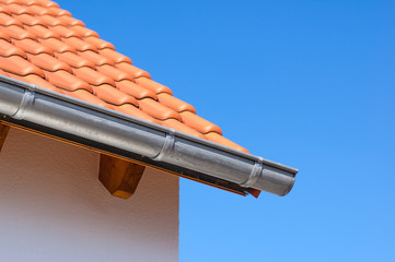 Corner of a house with gutters on a background of blue sky