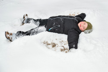 Fototapeta na wymiar Child playing in snow by making snow angel