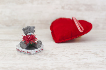 Miniature teddy bear and red heart on wooden background