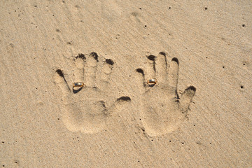Fototapeta na wymiar Hands print on sand with wedding rings. Wedding travel, beach marriage.