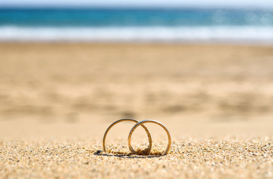 Wedding rings on sand, beach wedding travel copy space background.
