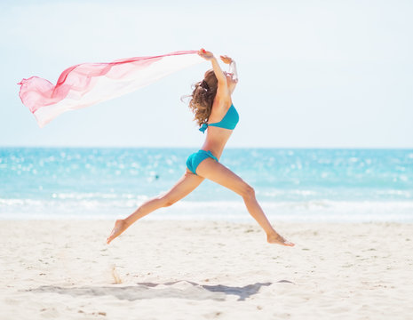 Young woman with parero jumping on beach