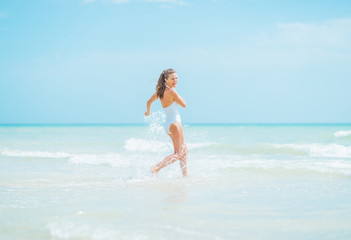 Smiling young woman in swimsuit running into sea
