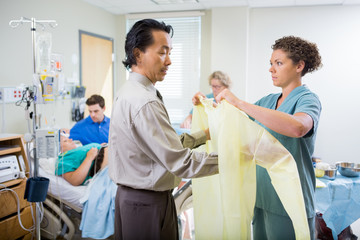 Nurse Assisting Doctor In Wearing Operation Gown At Hospital