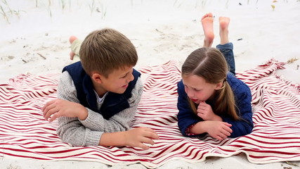 Siblings lying on blanket on the beach talking