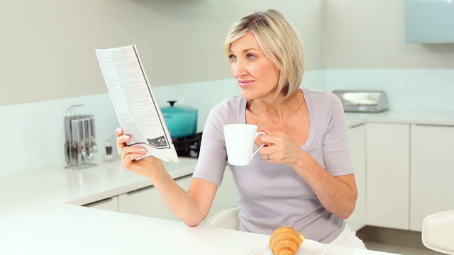 Blonde woman reading newspaper and drinking coffee