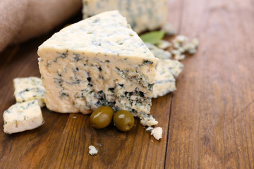 Tasty blue cheese with olives and basil, on wooden table
