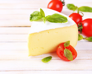 Tasty Camembert cheese with basil and tomatoes, on wooden table