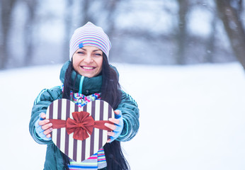 Beautiful brunette girl with heart shape box in the winter park.