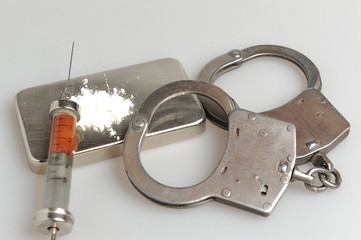 Drugs, syringe with blood, handcuffs on gray