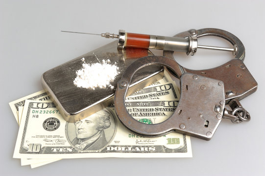Drugs, syringe with blood, handcuffs and money on gray